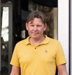 Portræt af Claus Hingeberg, indehaver og lystfiskerekspert hos Aarhus Fishing Gear, stående smilende foran butikken iført en gul polo.
